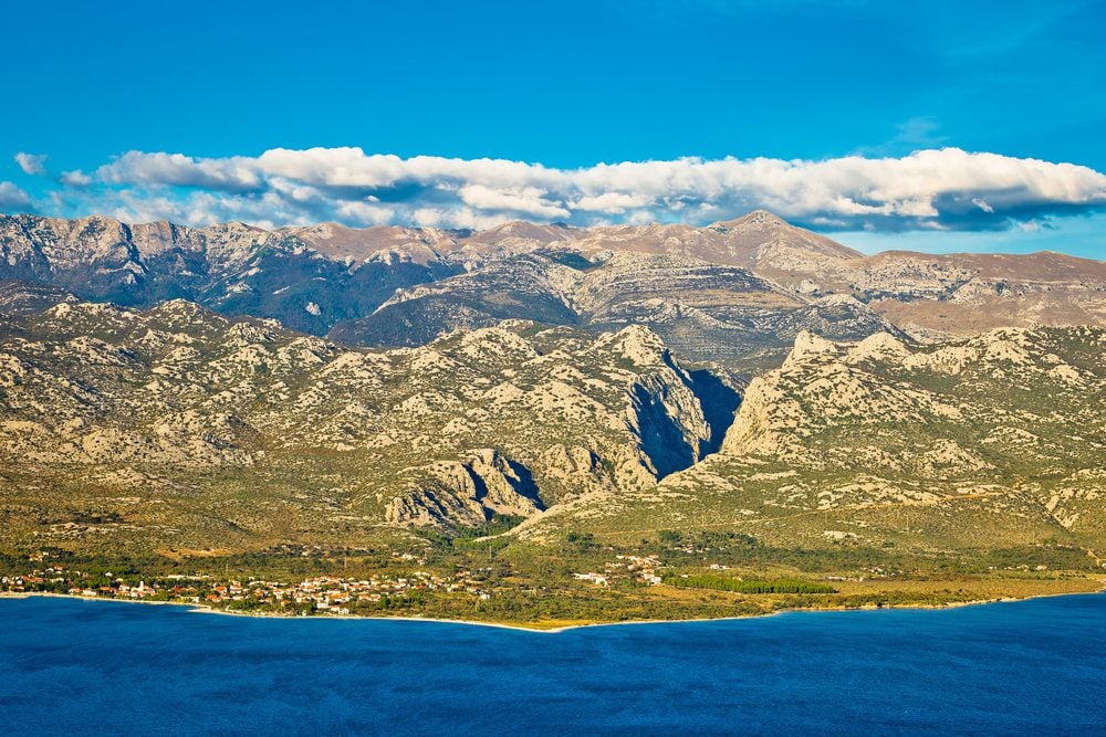 An ocean and mountain scene with a blue sky and some white clouds