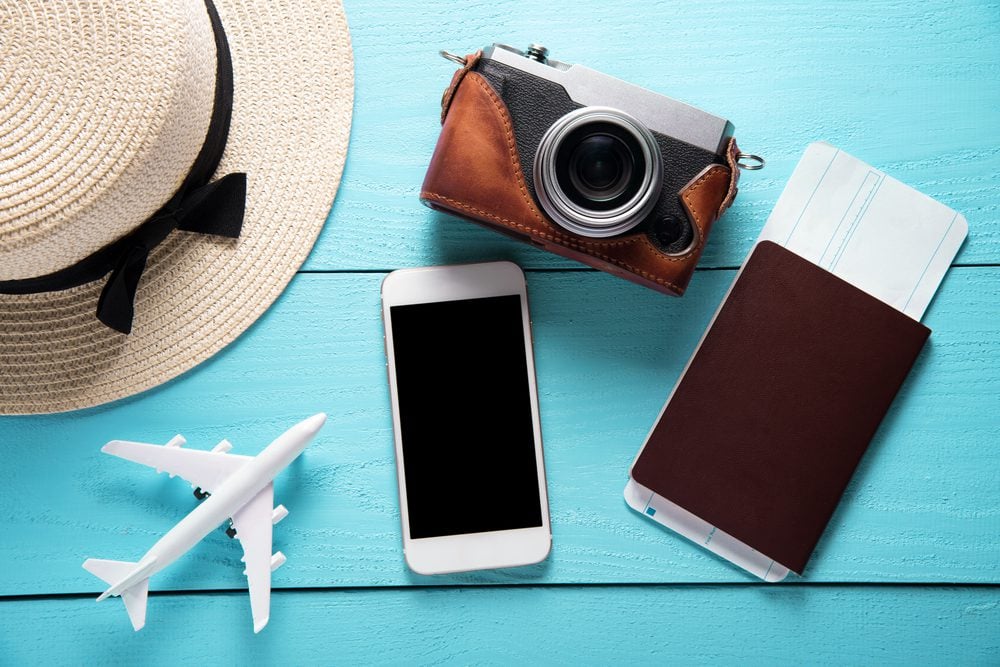 Phone, camera, hat, passport, and plane figurine on bright blue background